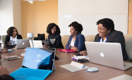 Four women in a meeting around a table, talking with laptops and paperwork in front of them