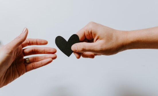 A hand holding a paper cut out of a heart and another hand reaching for it