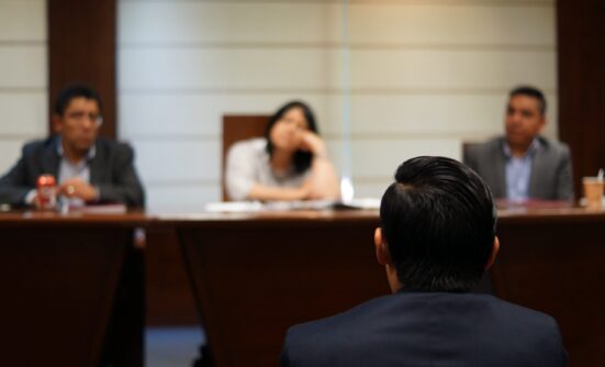 Blurred image of someone's back, sitting in front of a panel of three people