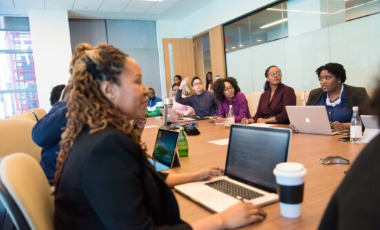 A group of women sitting around a table in a board room with their laptops