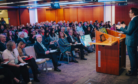 A photo showing audience members at the Reshaping Legal Services conference on 6 March 2025, with host Dean Dunham standing behind the podium on stage